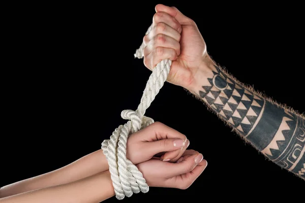 Partial view of man tying rope on female hands isolated on black — Stock Photo