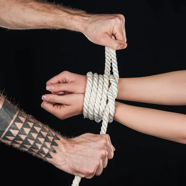 Close up of tattooed man tying rope on female hands isolated on black — Stock Photo