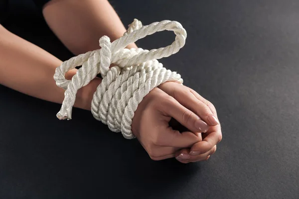 Cropped view of female bound hands on black background — Stock Photo