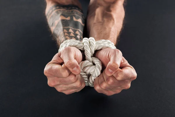Cropped view of male hands bound with rope isolated on black — Stock Photo