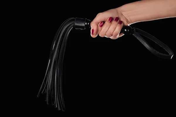 Обрізаний вид жіночої руки, що тримає шкіряний збитий батіг, ізольований на чорному — стокове фото