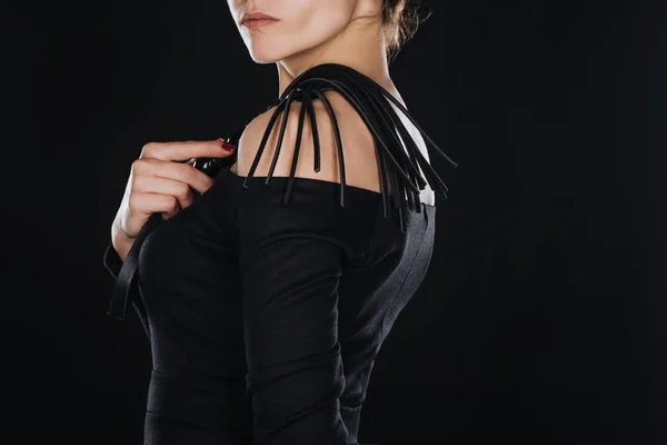 Vista lateral de la mujer sosteniendo látigo azotes de cuero aislado en negro - foto de stock