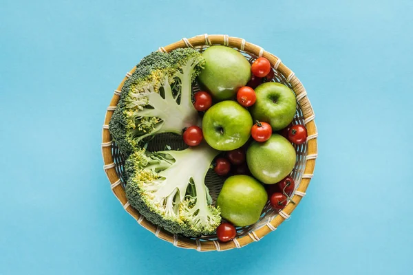Vista superior de legumes e maçãs em tigela de vime no fundo azul — Fotografia de Stock