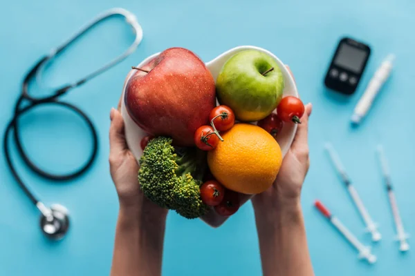 Frutas e legumes em mãos femininas com equipamento médico em fundo azul — Fotografia de Stock
