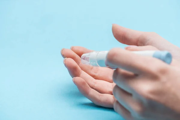 Vista recortada de las manos femeninas analizando el nivel de glucosa con aguja sobre fondo azul - foto de stock