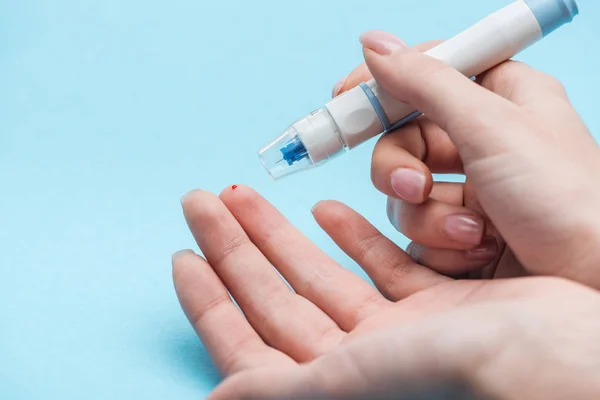 Ausgeschnittene Ansicht weiblicher Hände, die einen Glukosetest mit Nadel auf blauem Hintergrund durchführen — Stockfoto