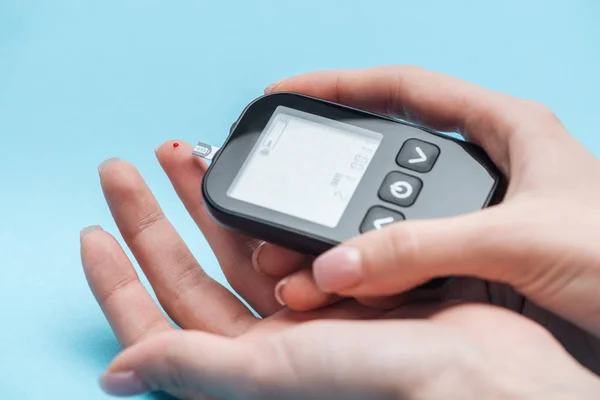 Cropped view of woman testing glucose level with glucometer on blue background — Stock Photo