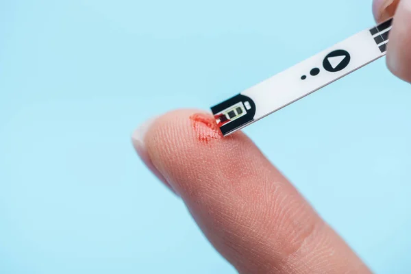 Close up of fingers and diabetes test strip isolated on blue background — Stock Photo