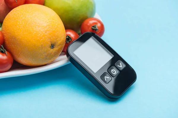 Close up view of glucometer with tomatoes and fruits on blue background — Stock Photo