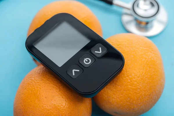 Vue rapprochée du glucomètre sur oranges avec stéthoscope sur fond bleu — Photo de stock