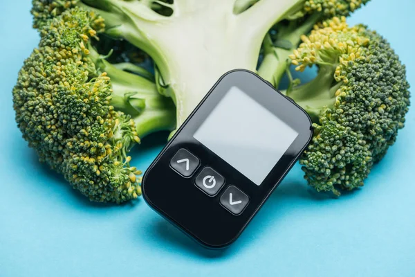 Vue rapprochée du glucomètre avec brocoli sur fond bleu — Photo de stock