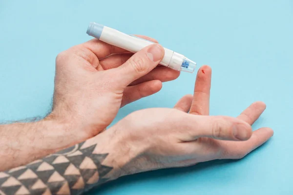 Cropped view of man testing glucose level with syringe on blue background — Stock Photo