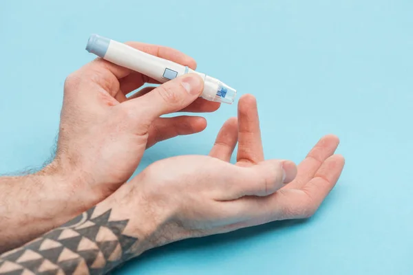 Partial view of man doing glucose level test with needle on blue background — Stock Photo