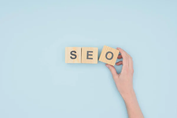 Top view of female seo manager holding cube with seo lettering on light blue background — Stock Photo