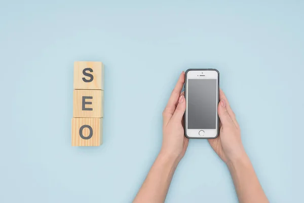 Top view of woman holding smatphone near wooden blocks on light blue background — Stock Photo