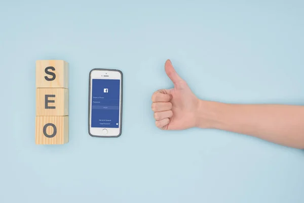 Visão superior do gerente seo feminino colocando polegares para cima perto do smartphone com o aplicativo facebook no fundo azul claro — Fotografia de Stock