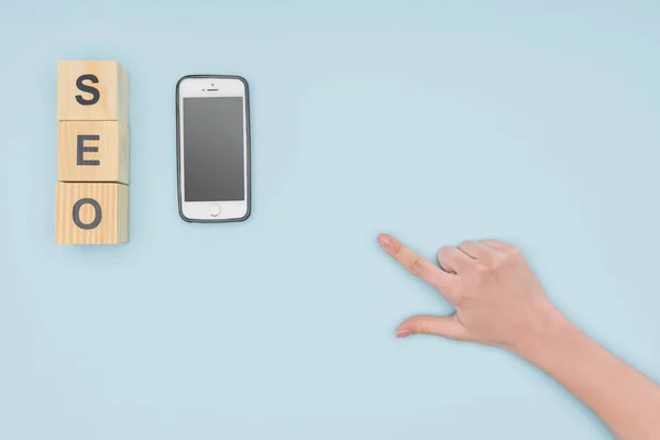 Top view of female hand pointing at smartphone and wooden cubes on light blue background — Stock Photo