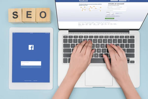 Draufsicht auf Frau tippt auf Laptop-Tastatur in der Nähe digitales Tablet mit Facebook-Website auf hellblauem Hintergrund — Stockfoto