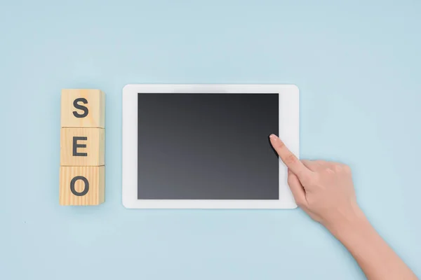 Top view of female seo manager pointing at digital tablet near wooden cubes  on light blue background — Stock Photo