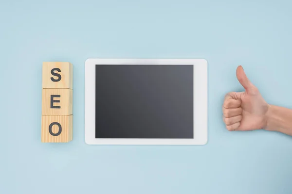 Top view of woman showing thumbs up near gadget and cubes  on light blue background — Stock Photo