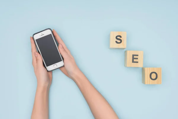 Vista superior de la mujer sosteniendo el teléfono inteligente sobre fondo azul claro - foto de stock