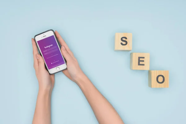 Vista superior de la mujer sosteniendo teléfono inteligente con aplicación instagram sobre fondo azul claro - foto de stock