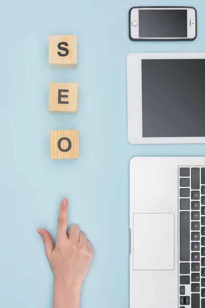 Vista superior de la mujer apuntando a cubos de madera cerca de gadgets sobre fondo azul claro - foto de stock