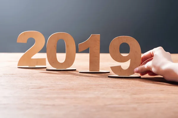 Vista recortada de la mujer ajustando 2019 fecha hecha de números de madera contrachapada en la mesa de madera con fondo negro - foto de stock