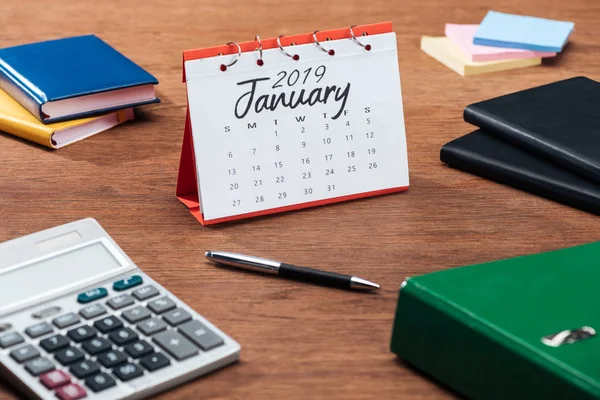 Janeiro 2019 calendário, calculadora e artigos de papelaria em mesa de escritório de madeira — Fotografia de Stock