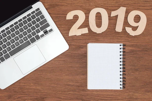 Top view of wooden desk with laptop, empty notebook and 2019 date made of plywood — Stock Photo