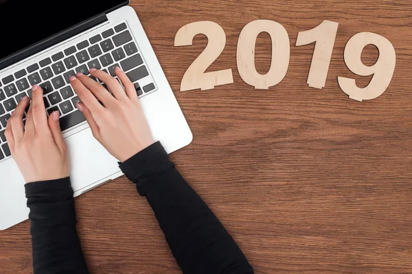 Cropped view of woman using laptop at wooden table with 2019 date made of plywood — Stock Photo