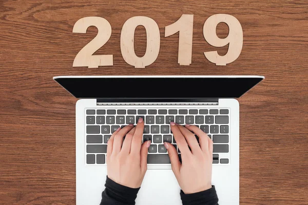 Cropped view of woman using laptop at wooden table with 2019 date made of plywood — Stock Photo