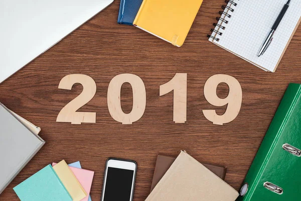 Top view of wooden office desk with notebooks, smartphone and 2019 date made of plywood — Stock Photo