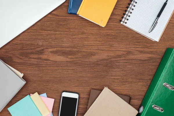 Top view of wooden office desk with notebooks and smartphone with blank screen — Stock Photo