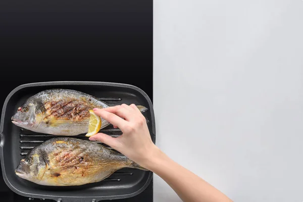 Recortado tiro de persona exprimiendo limón mientras freír pescado - foto de stock