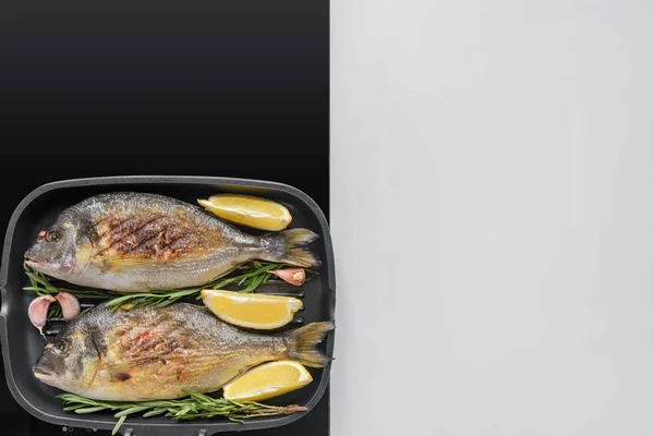 Вид вкусной жареной рыбы с розмарином, лимоном и чесноком на электрической плите — стоковое фото