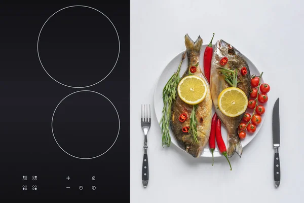 Delicious fried fish with cherry tomatoes, rosemary, chili peppers and lemon on plate with fork and knife — Stock Photo