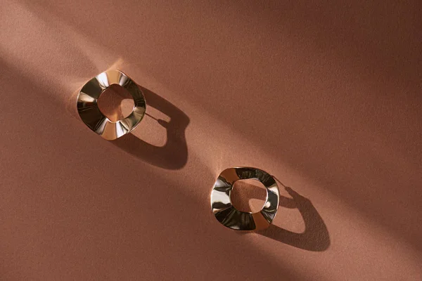 Вид зверху на красиві розкішні золоті сережки на коричневій поверхні з сонячним світлом — стокове фото