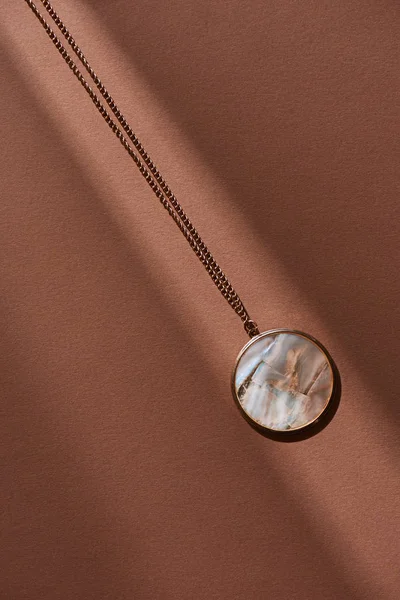 Вид сверху на красивый круглый медальон с мрамором на коричневой поверхности с солнечным светом — стоковое фото