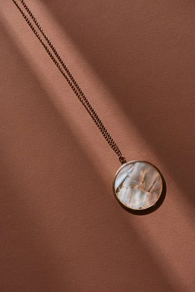 Top view of beautiful round locket with marble on brown surface with sunlight — Stock Photo