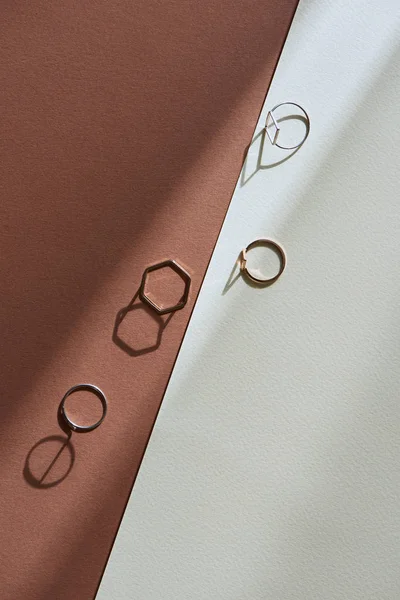 Vista superior de belos anéis dourados de luxo na superfície marrom e branca com luz solar — Fotografia de Stock