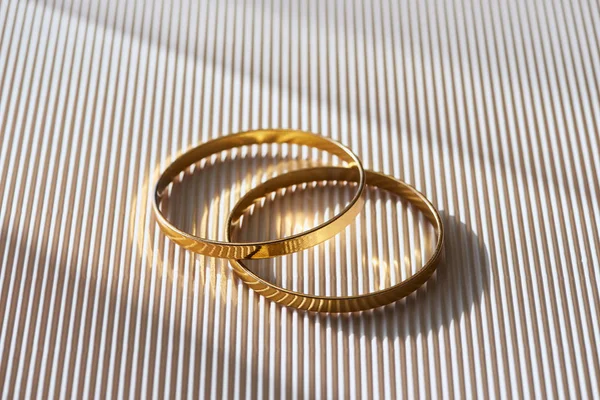 Крупным планом красивые роскошные обручальные кольца на полосатой белой поверхности с солнечным светом — стоковое фото