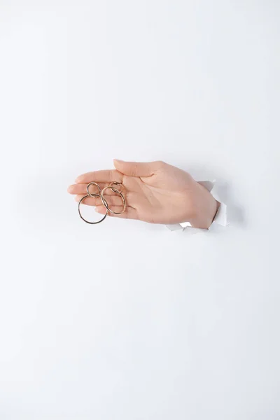 Cropped image of woman holding hand with beautiful round golden earrings through white paper — Stock Photo