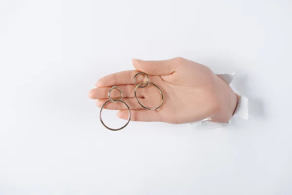 Cropped image of woman holding hand with beautiful round earrings through white paper — Stock Photo