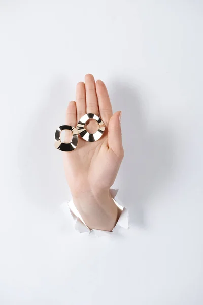 Cropped image of woman holding hand with beautiful black and white earrings through white paper — Stock Photo