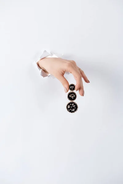 Immagine ritagliata di donna che si tiene per mano con bellissimo orecchino costoso con diamanti brillanti attraverso carta bianca — Foto stock