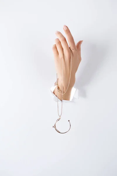 Imagen recortada de la mujer cogida de la mano con hermoso collar de lujo a través de papel blanco - foto de stock