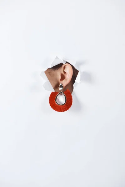 Image recadrée de femme avec belle boucle d'oreille rouge de luxe debout dans le trou de papier blanc — Photo de stock