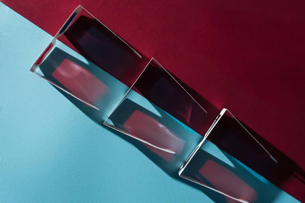 Vue du dessus des verres en carton 3d en rangée avec des ombres sur fond bleu et bordo — Photo de stock