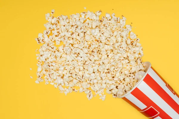 Top view of overturned striped bucket with popcorn isolated on yellow — Stock Photo